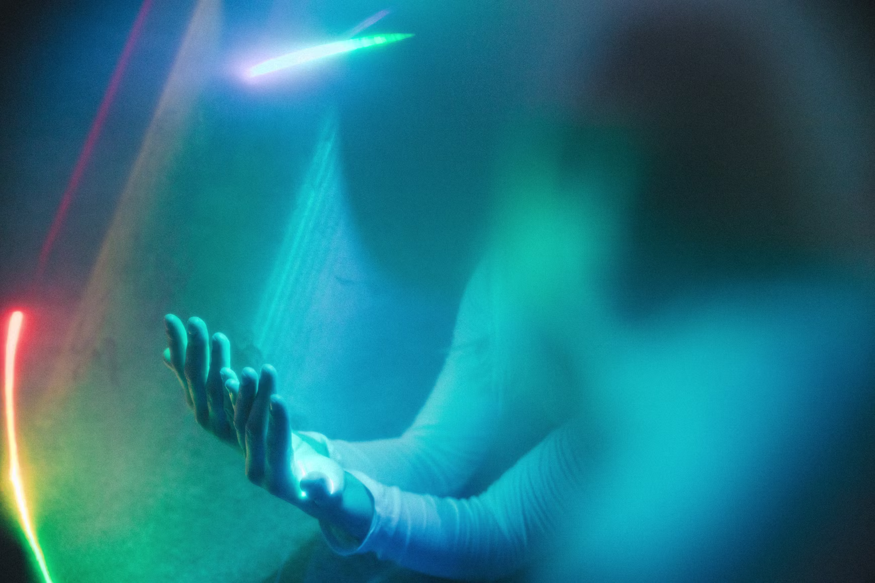 A figure reaching toward a softly lit wall in coloured light, motion slightly blurred.
